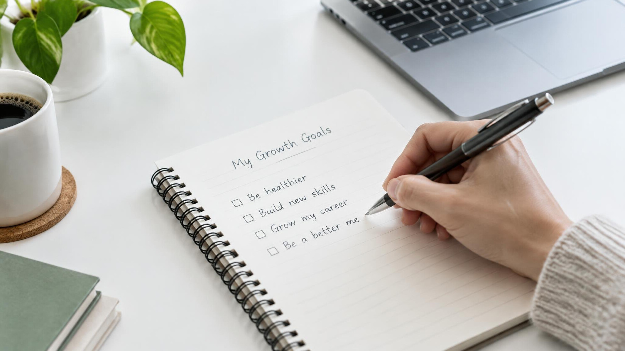 Hand writing goals in a notebook planner on a desk